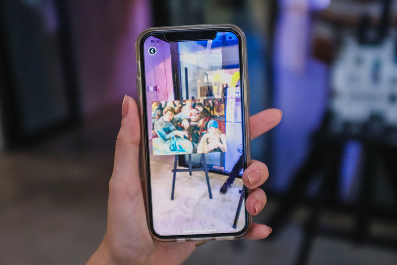 Exhibition visitor holding a phone showing an artwork in the app