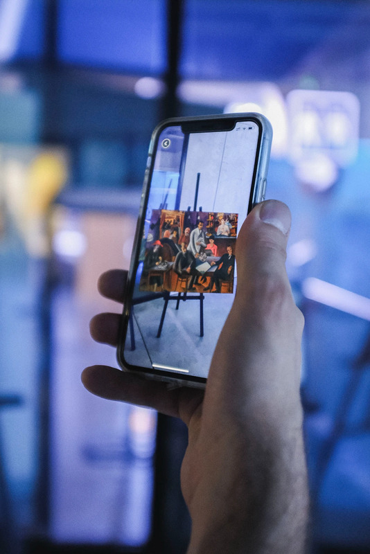 Exhibition visitor holding a phone showing an artwork in the app