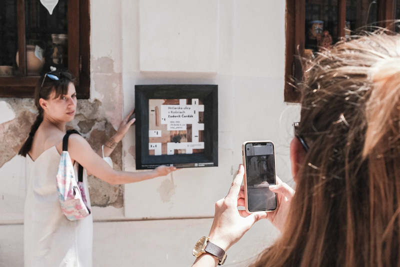 Exhibition visitor photographing another visitor next to an app marker on the wall